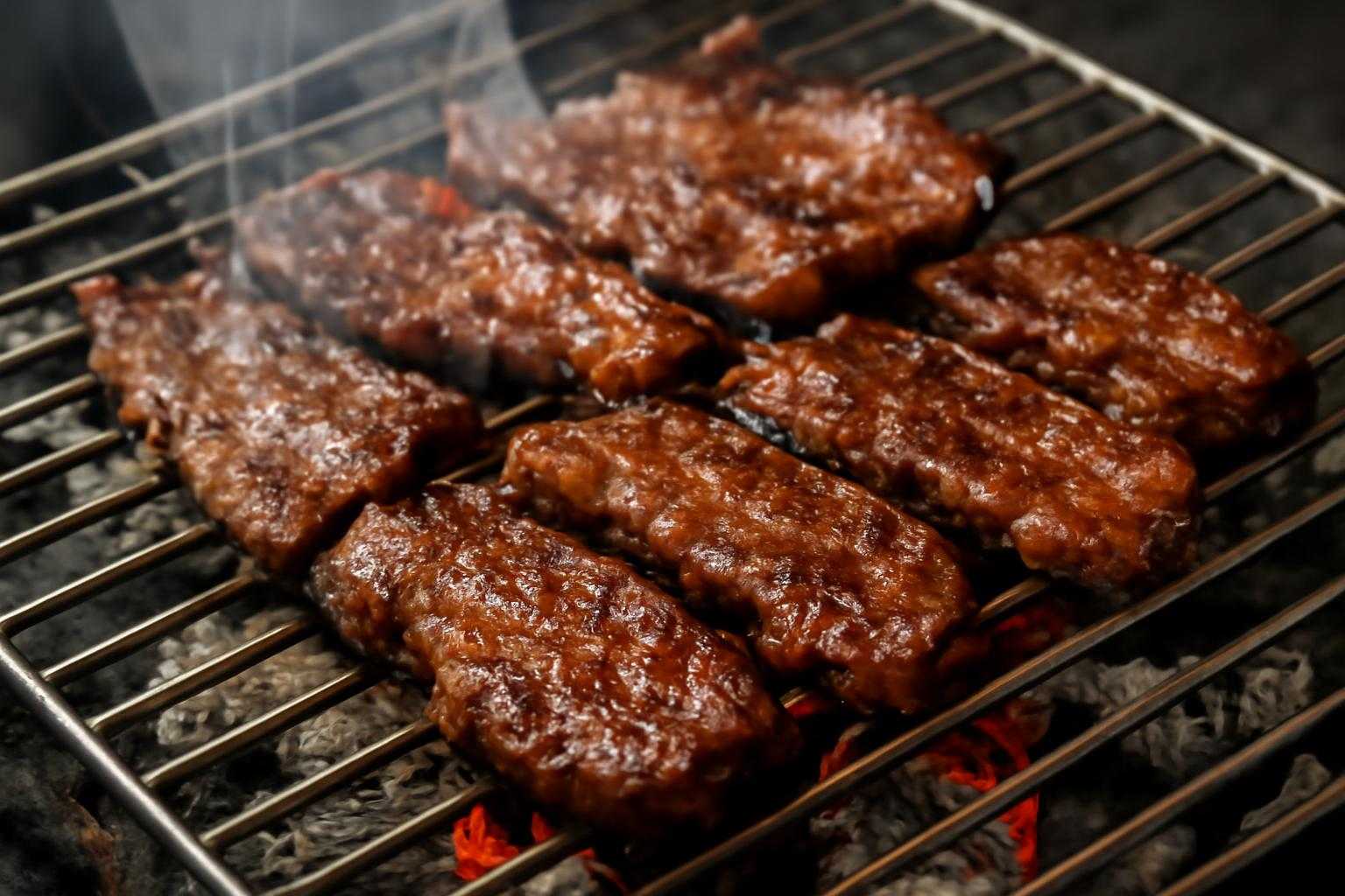 焼き網の上でハラミを焼く様子。焼き色がついた肉と炭火を表現