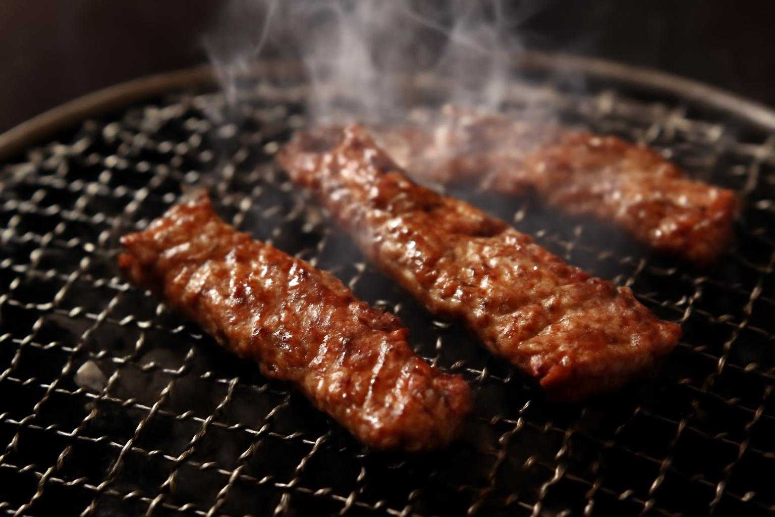 牛サガリを焼き網の上で焼いている、湯気が立ち上る調理風景